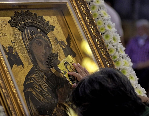 A member of the faithful touches a prayer card to the icon of Our Mother of Perpetual Help at Baclaran Church in Parañaque City, Metro Manila. (Photo by Elmarc Lim/CBCP News)