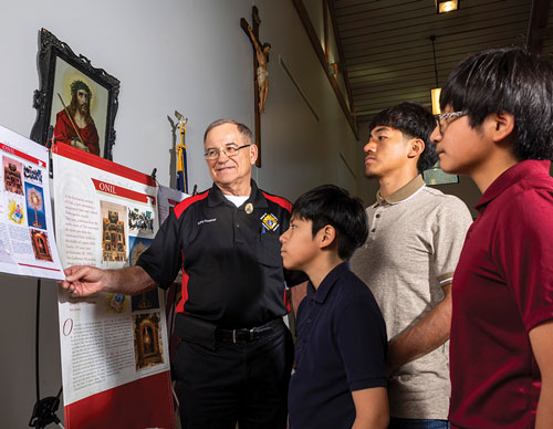 Larry Koerner, state faith director and a member of Victor Vifquain Council 7704 in Crete, Neb., shows young parishioners one of the Eucharistic miracles detailed in a bilingual exhibit at Sacred Heart Parish in Crete. (Photo by Kenneth Ferriera)