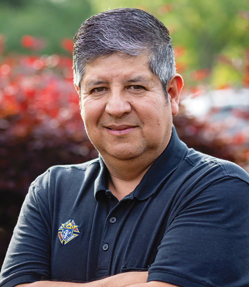 Man poses with his arms crossed in a navy blue polo shirt