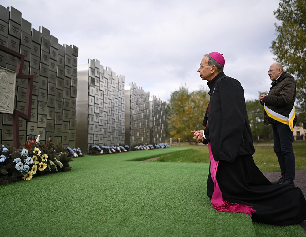 Supreme Chaplain Archbishop William Lori prays Oct. 19 at a memorial that marks the graves of 119 victims of the 2022 Bucha massacre on the grounds of St. Andrew the First-Called Church in Bucha, Ukraine. Volodymyr Ostapchuk (right), a member of Blessed Nicholas Charnetsky Council 16890 in Irpin, was present in Bucha during the Russian occupation and guided the supreme chaplain during his visit. (Photo by Andrii Gorb)