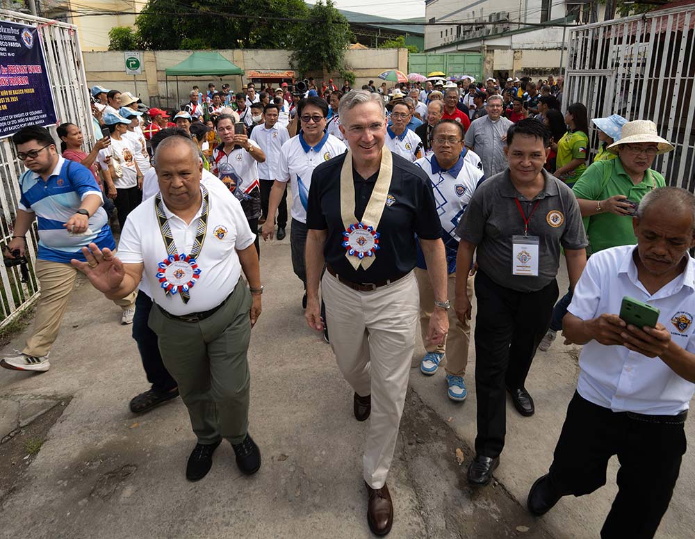 Supreme Knight Patrick Kelly and Luzon South Deputy Danilo Sanchez (front left) lead a crowd of Knights onto the grounds of Santo Niño de Baseco Parish in Manila, Philippines, where local Knights sponsor food distribution and other charitable programs. Hanging from their necks are welcome badges featuring the word “Mabuhay,” a traditional Filipino greeting. (Photo by Tamino Petelinšek)